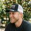 Side profile of laughing model wearing black front and white mesh contrast trucker cap