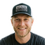 Man wearing black and white trucker snapback hat with embroidered BECAUSE I'M A GIVER patch