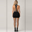Rear view showcasing low-cut open back, branded vertical backstrap, short hemline, black fishnet stockings, and chunky boots