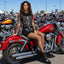 Side profile of model seated on red motorcycle displaying skeleton graphic on front of mini dress in sunny parking lot