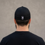 Rear view of black hat showing mesh back and small white embroidered face logo at crown base
